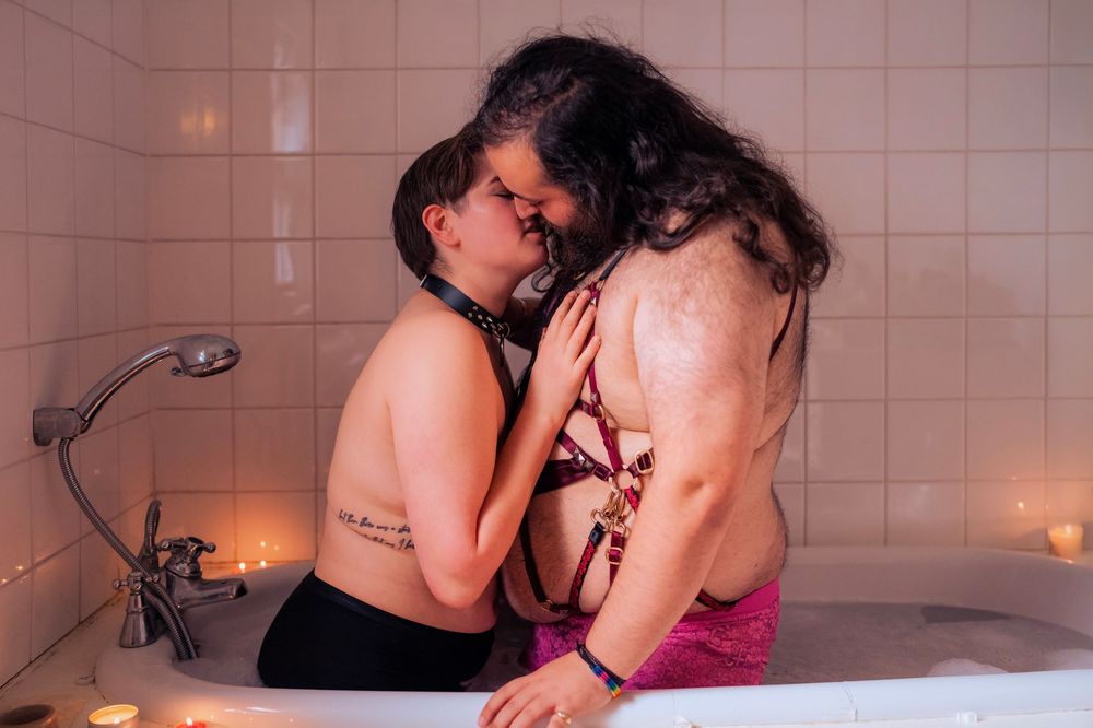 Two people sharing an intimate moment together in a candlelit bathtub in a tiled bathroom.
