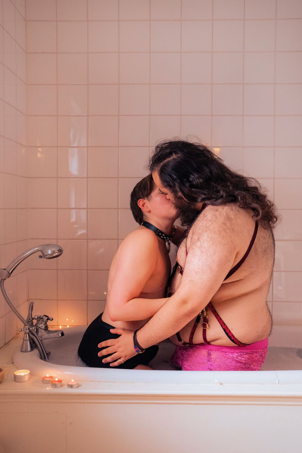 Two people sharing an intimate kiss while sitting in a bathtub with candles, wearing lingerie.