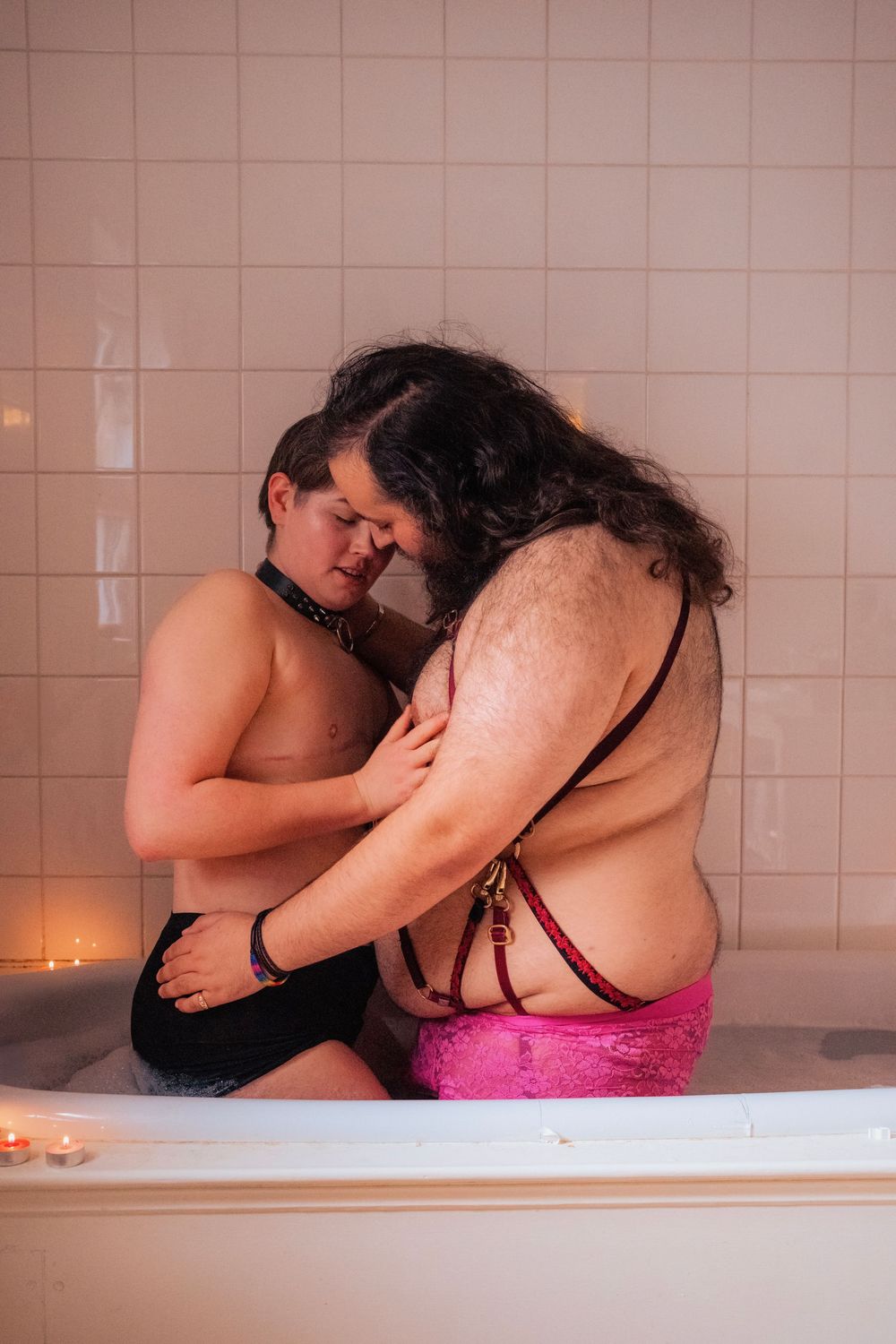 Two people sharing an intimate moment together in a bathtub, with candles glowing softly in the background.