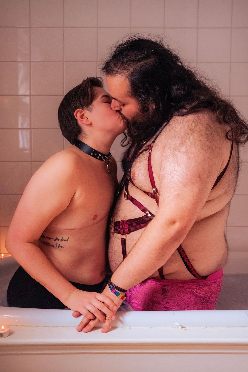 Two people sharing a kiss while embracing intimately near a bathtub in a tiled bathroom.