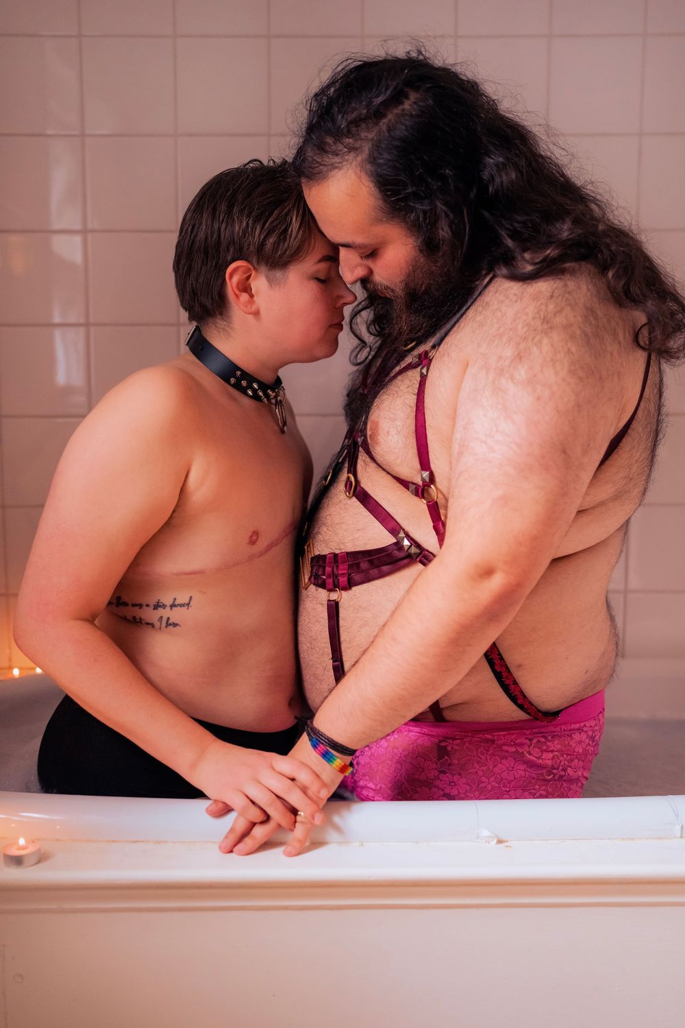Two people sharing an intimate moment together near a bathtub in a warmly lit bathroom.
