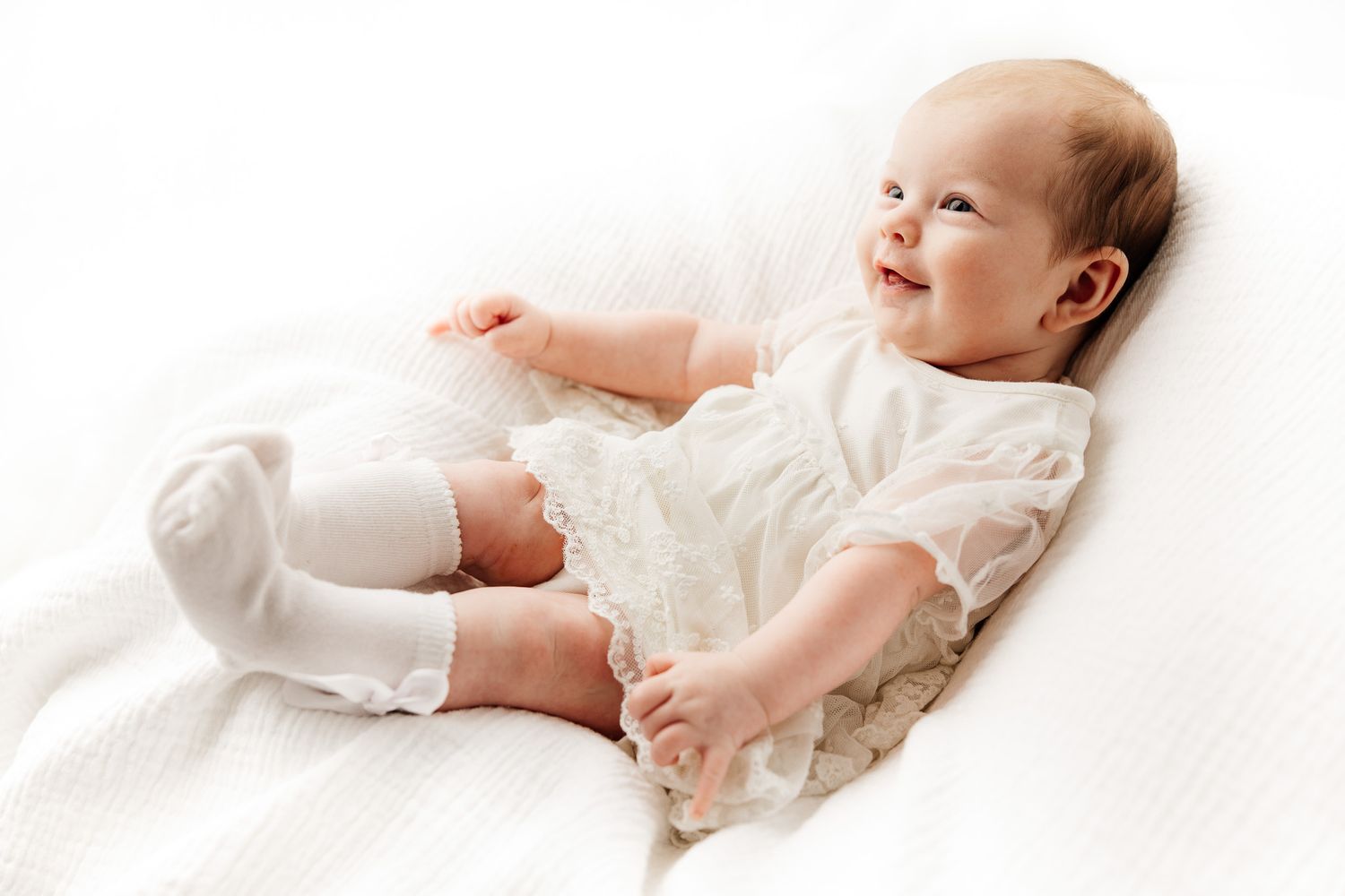 Smiling baby with rosy cheeks lying down, looking up with bright eyes and a joyful expression on a white background.
