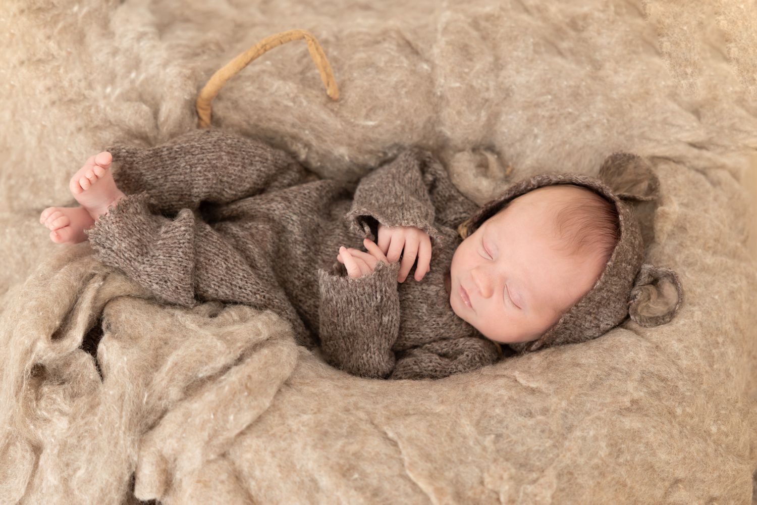 Sleeping newborn baby in brown knit bear romper and hat on soft tan textured blanket.