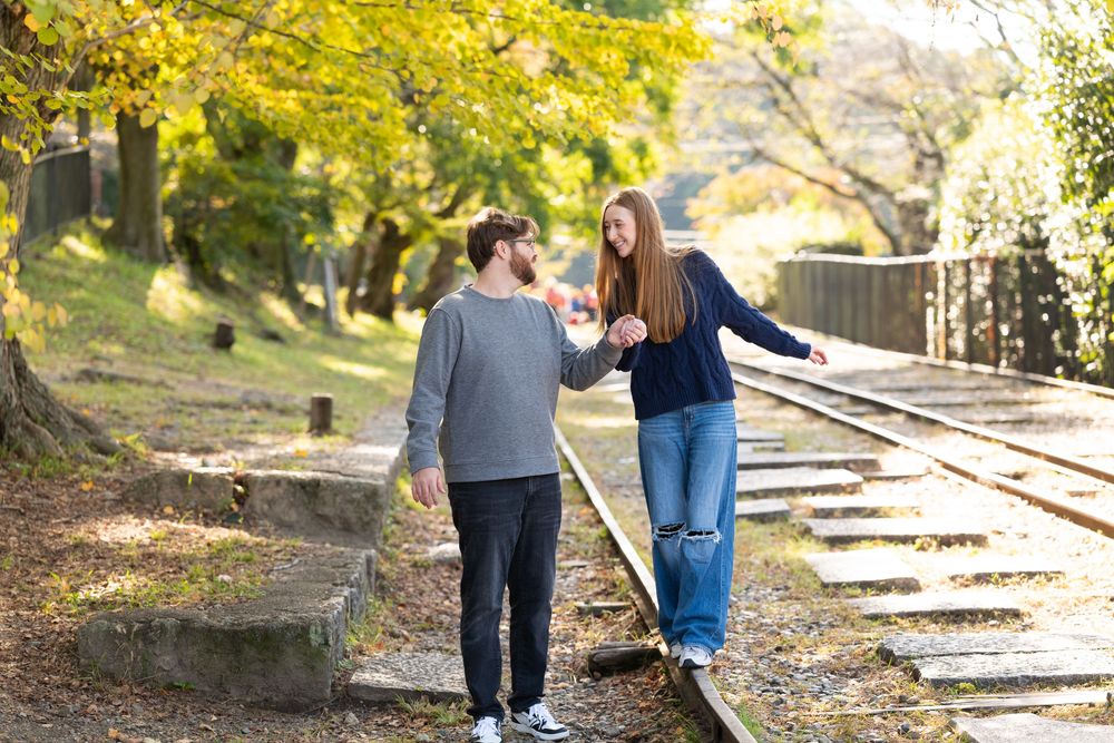Couple holding hands and walking along a railway track surrounded by golden autumn trees on a sunny day.