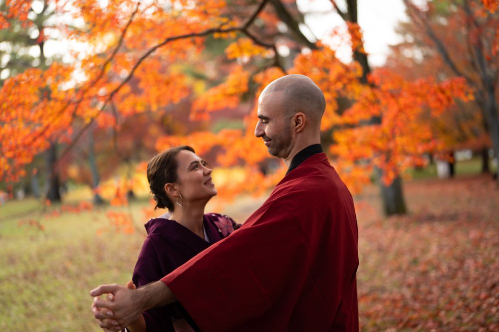 Couple embracing and smiling at each other beneath vibrant orange autumn maple trees in a peaceful park.