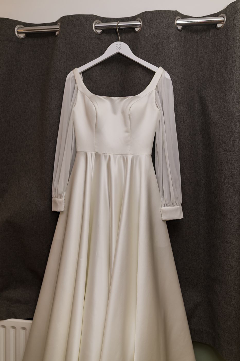 Elegant ivory satin A-line wedding dress with sheer sleeves and square neckline hanging on a white hanger.