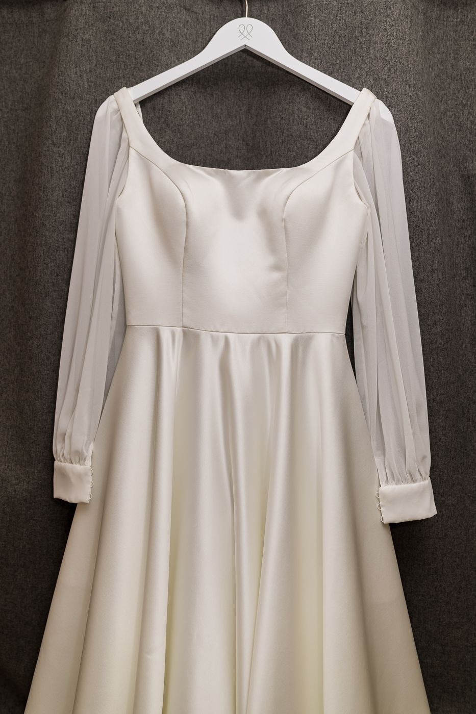 Elegant ivory satin wedding dress with sheer long sleeves and square neckline displayed on a white hanger.