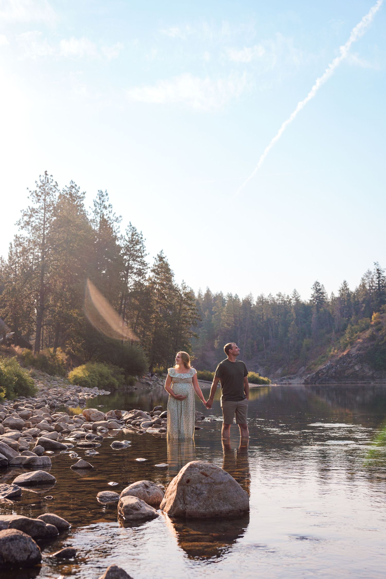 A pregnant woman stands peacefully in the woods, bathed in the warm glow of a sunset.