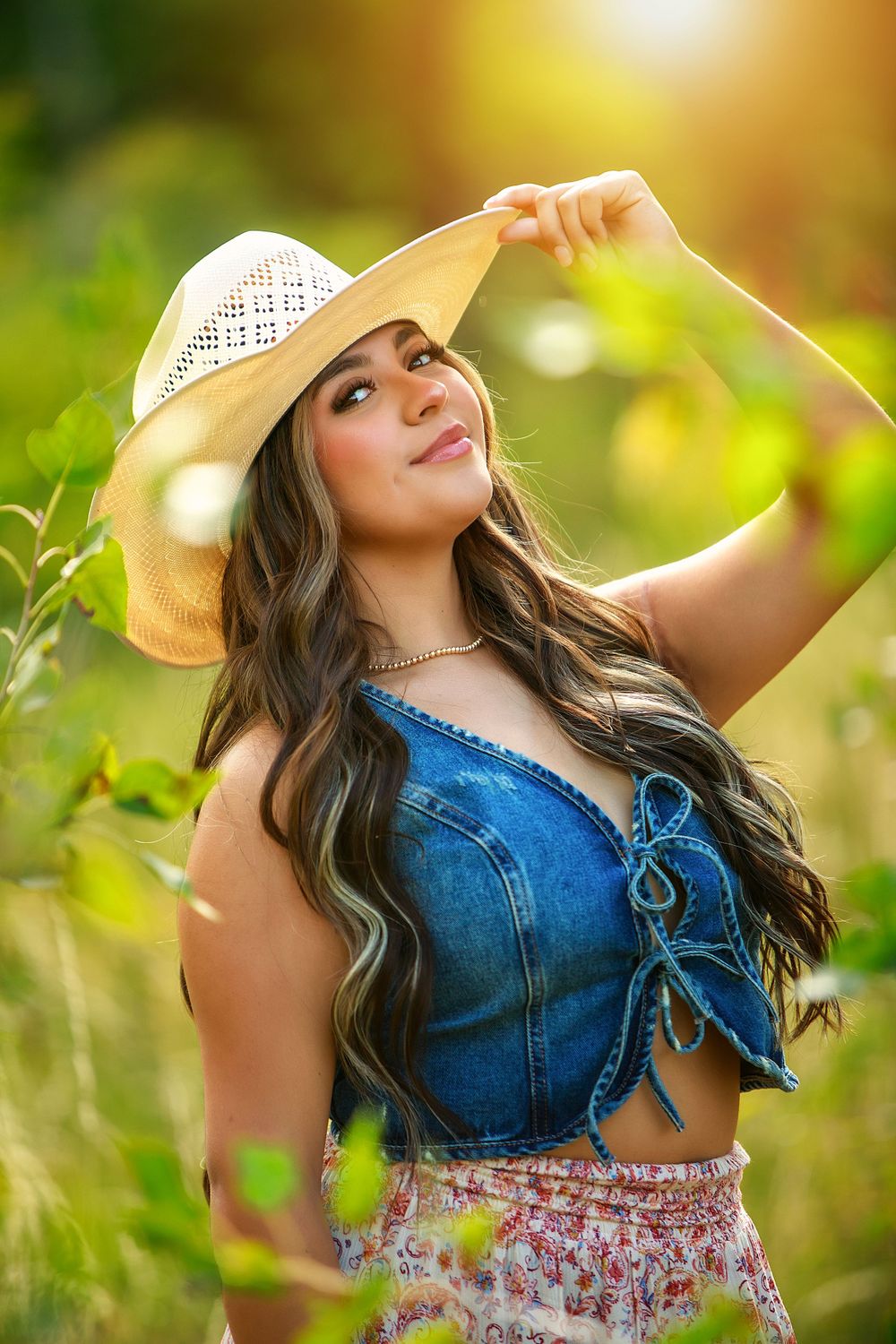 Summer portrait of someone in a denim top and sun hat among sunlit foliage.
