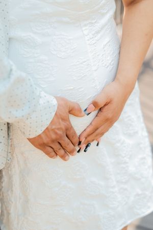 Close-up of bride and groom holding hands, showcasing black and blue manicured nails against white lace wedding dress.