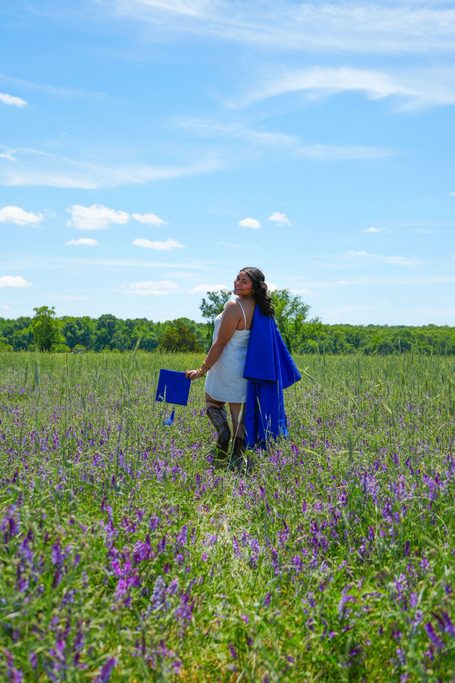 Pregnant woman in white shirt with partner's hands cradling baby bump outdoors on sunny day.