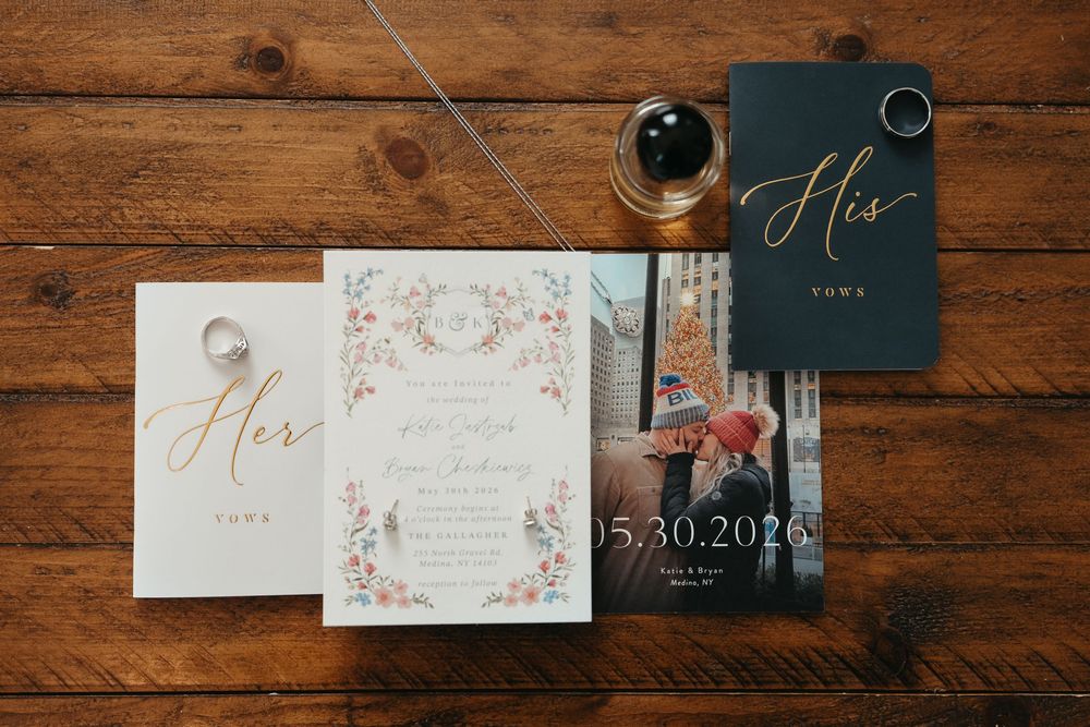 Elegant wedding stationery suite with floral invitation, His and Her vow books, rings, and a couple photo on rustic wood.