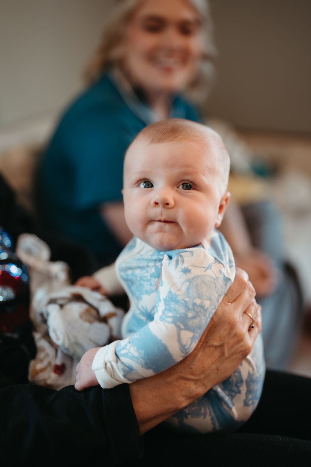 A smiling nurse holds an alert baby in a blue floral onesie during a pediatric checkup visit.