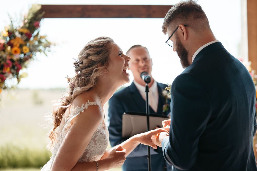 Bride and groom exchange rings at the altar during an outdoor wedding ceremony with colorful floral arrangements.