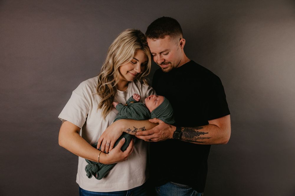 A couple tenderly gazes at their newborn baby wrapped in green during a studio newborn photography session.