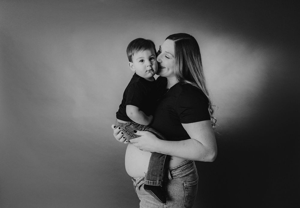 Black and white maternity photo of a pregnant woman holding a toddler boy, sharing a tender moment together.