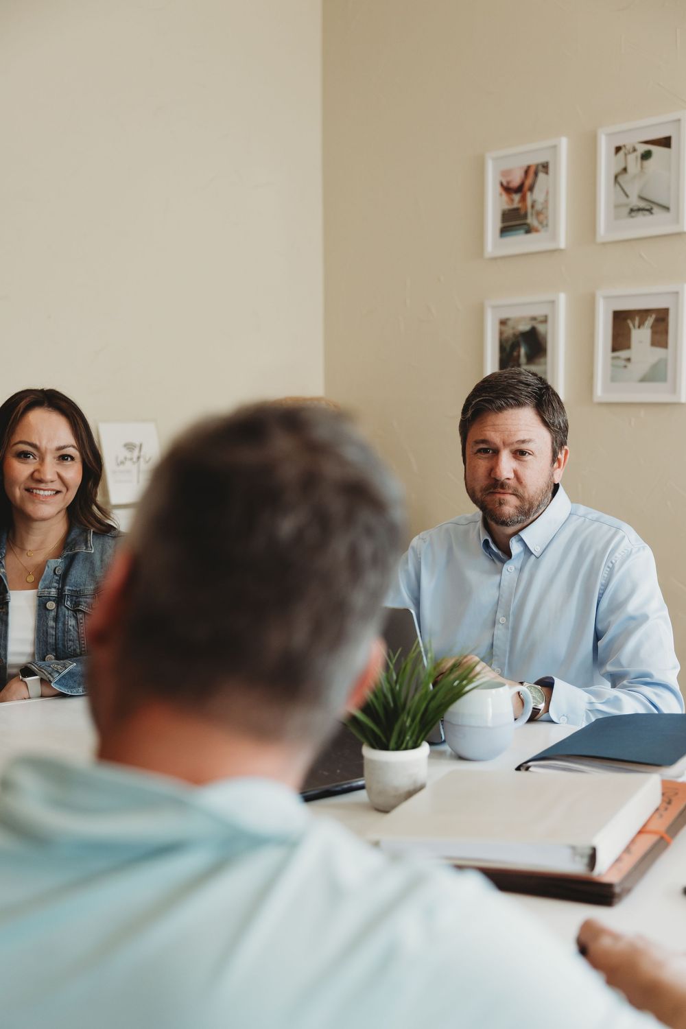 Three colleagues engaged in a productive office meeting around a conference table with notebooks and a laptop.