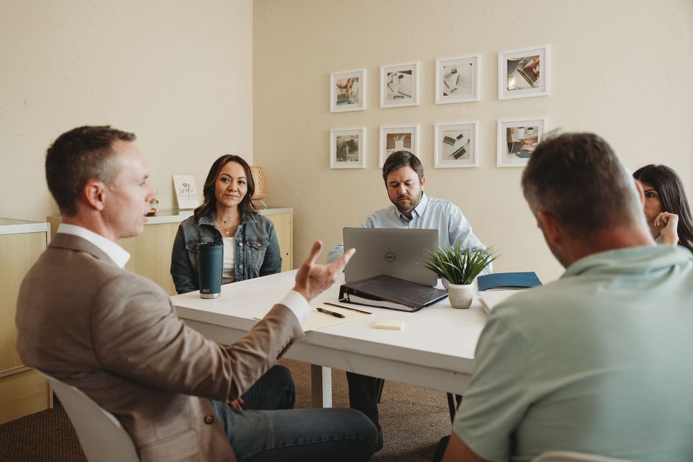 Five professionals engaged in a collaborative business meeting around a conference table with a laptop.