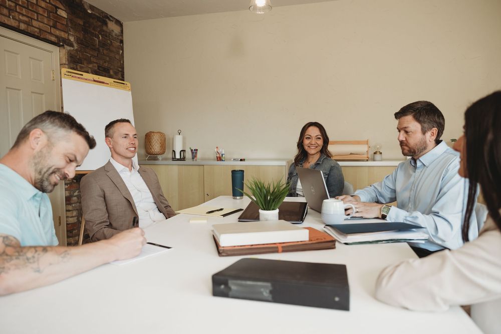 Five professionals engaged in a productive business meeting around a white conference table in a modern office.