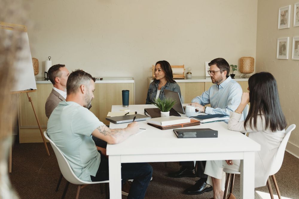 Five colleagues collaborate around a white conference table in a bright, modern office meeting room.