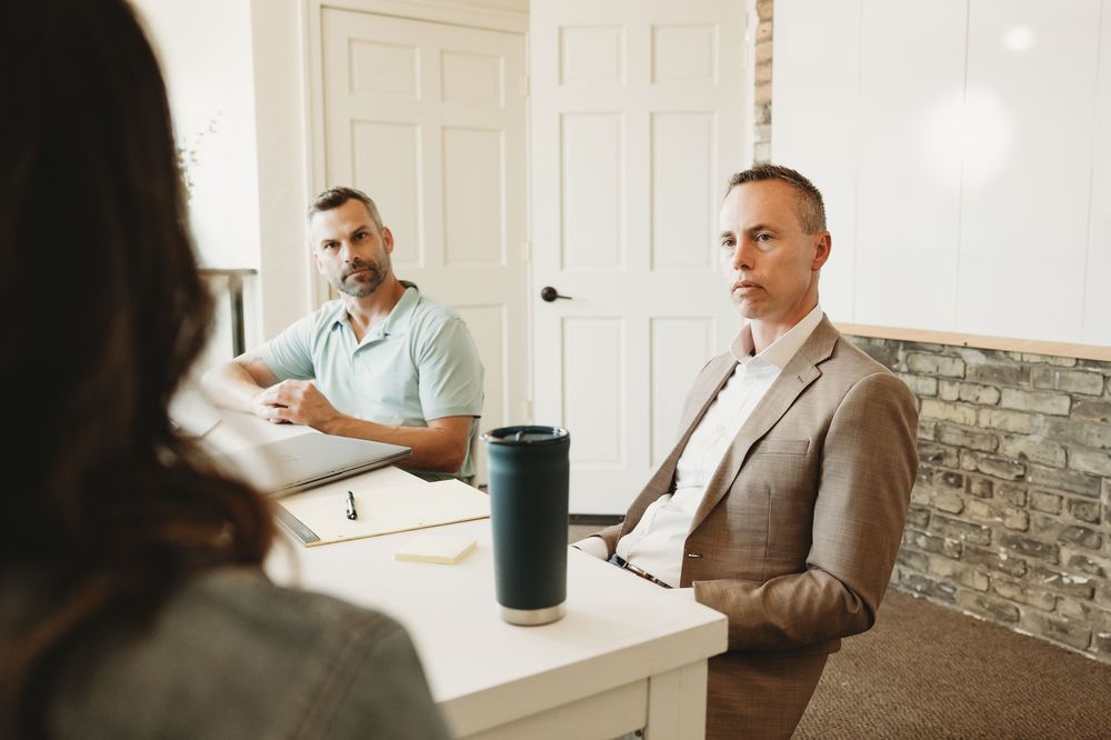 Two businessmen sitting at a table in a modern office during a professional meeting or interview.