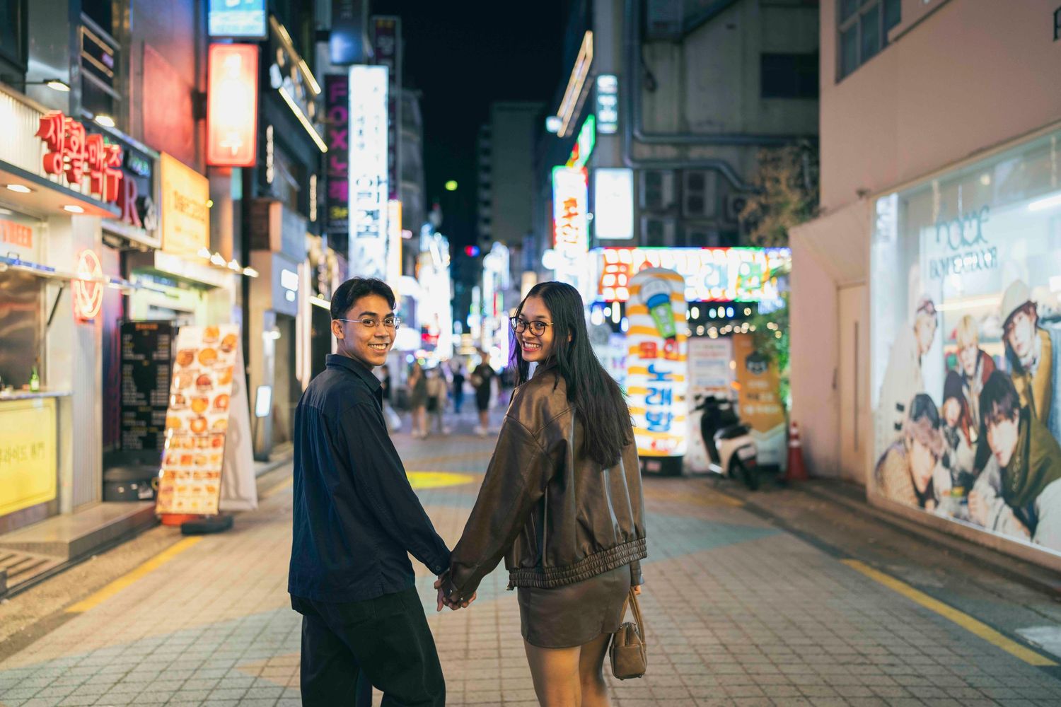 Couple holding hands on a vibrant night street in Asia, surrounded by neon signs and city lights.