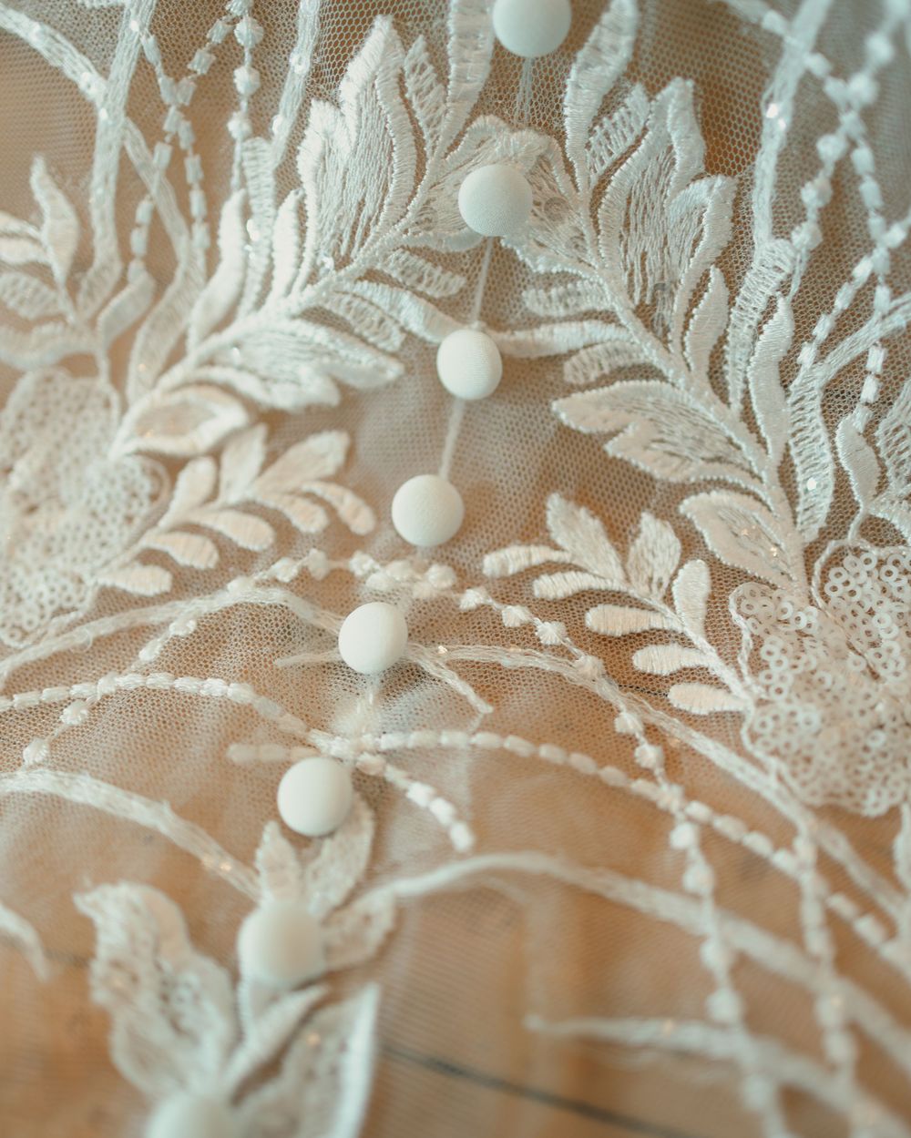 Close-up of delicate ivory lace fabric with floral embroidery and pearl button details on sheer tulle.