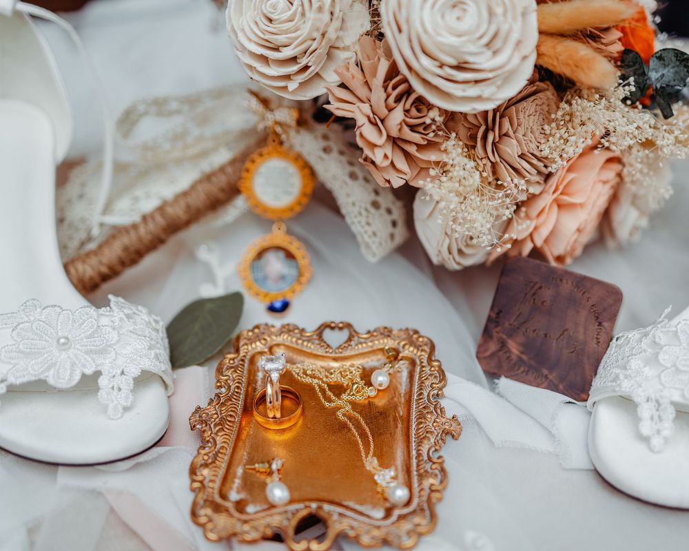 Elegant wedding flat lay with blush floral bouquet, gold ornate tray, pearl jewelry, perfume bottle, and white lace heels.