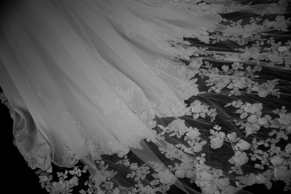 Black and white close-up of a wedding dress with delicate floral lace detail spread across the floor.