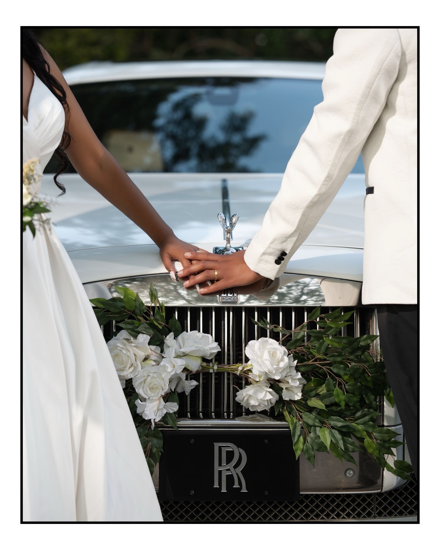 Bride and groom holding hands in front of a Rolls-Royce decorated with white roses at a wedding.