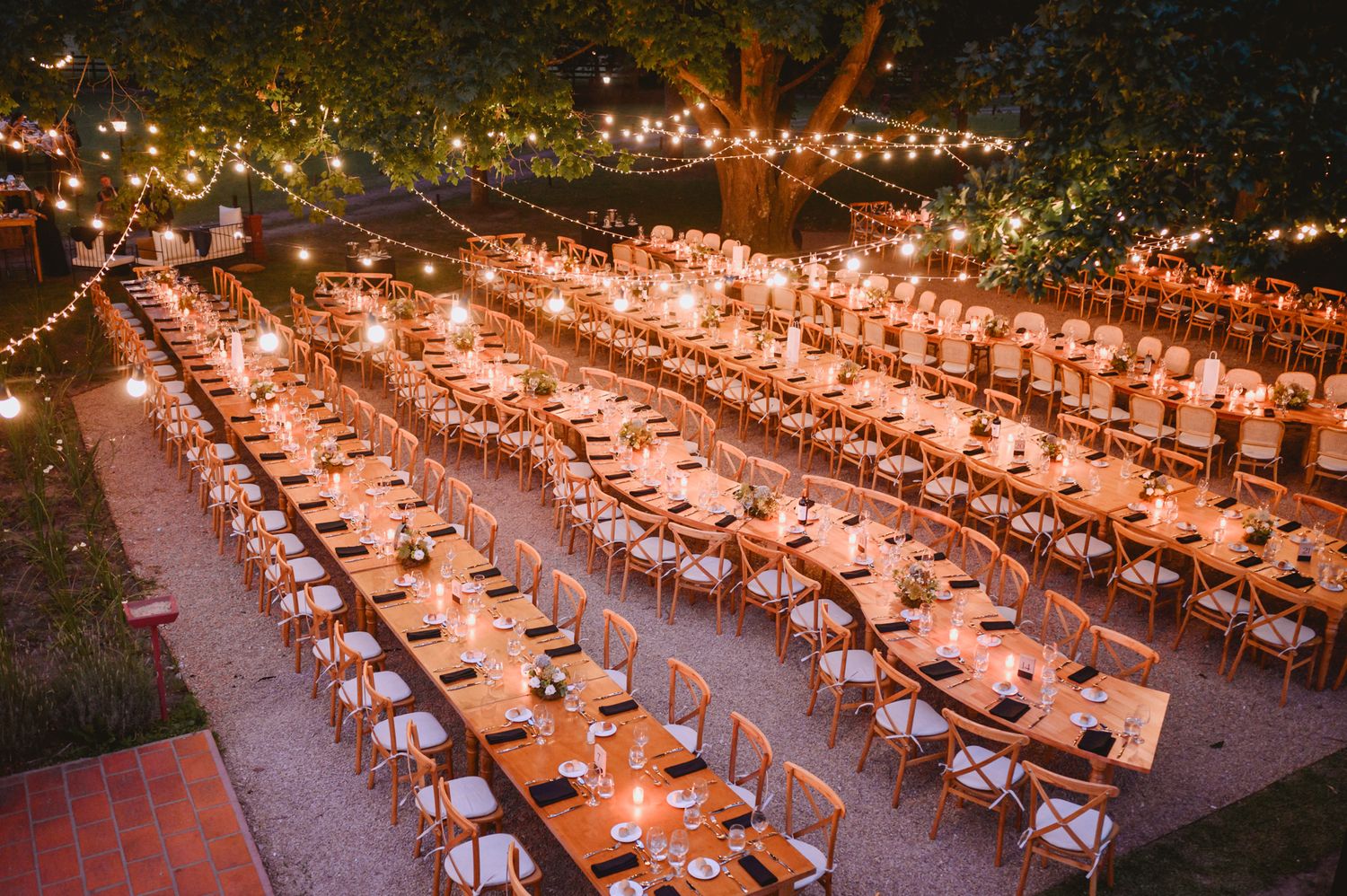 Overhead view of an elegant outdoor evening wedding dinner with string lights and long tables.