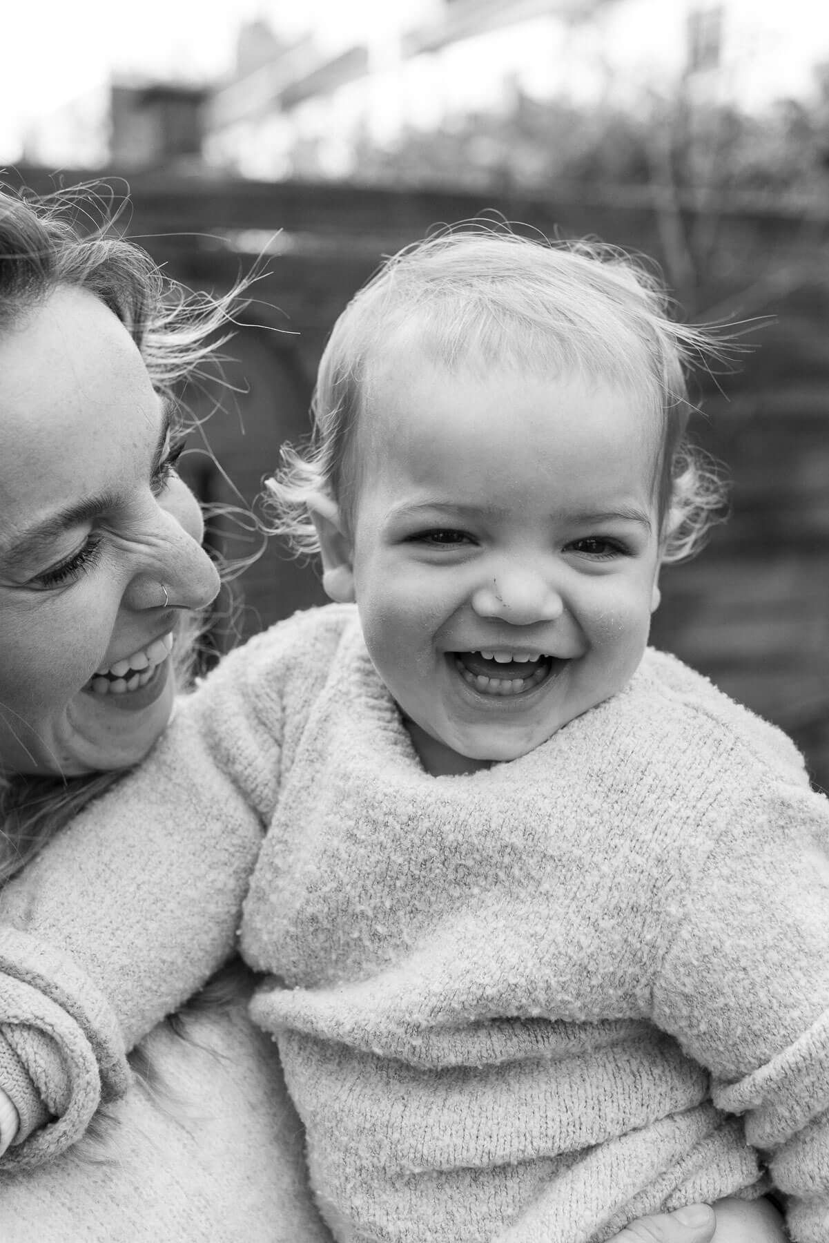 Black and white photo of a laughing baby being held by a smiling woman, photographed during a family photo shoot in Brighton