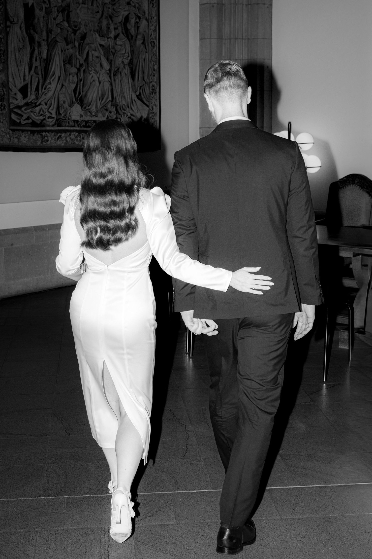 Black and white photo of an elegant couple walking away, woman in white dress, man in dark suit.