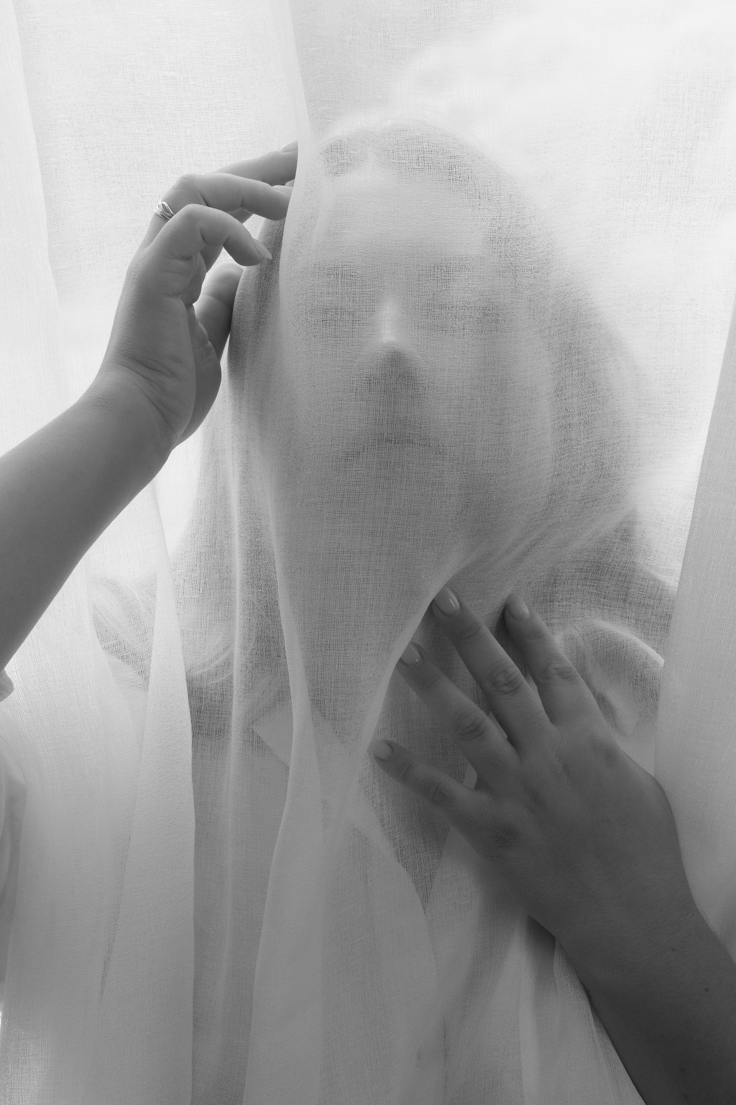 Portrait artistique en noir et blanc derrière un voile translucide.