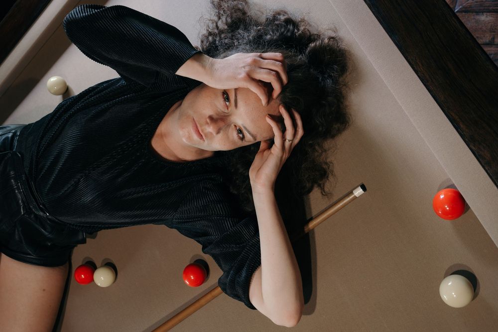 Portrait d’une femme allongée sur un billard, entourée de boules, dans une composition graphique.