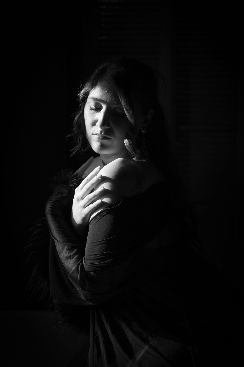 Portrait en clair-obscur d’une femme vêtue de noir, éclairée latéralement dans une ambiance intimiste.