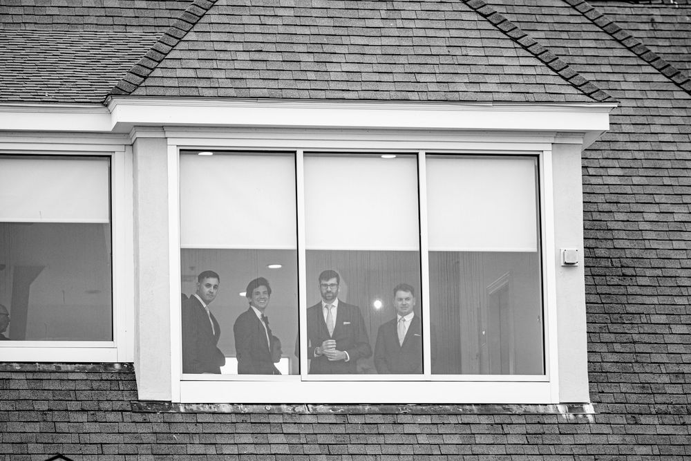 Four men in suits standing behind large windows on an upper floor, viewed from outside in black and white.