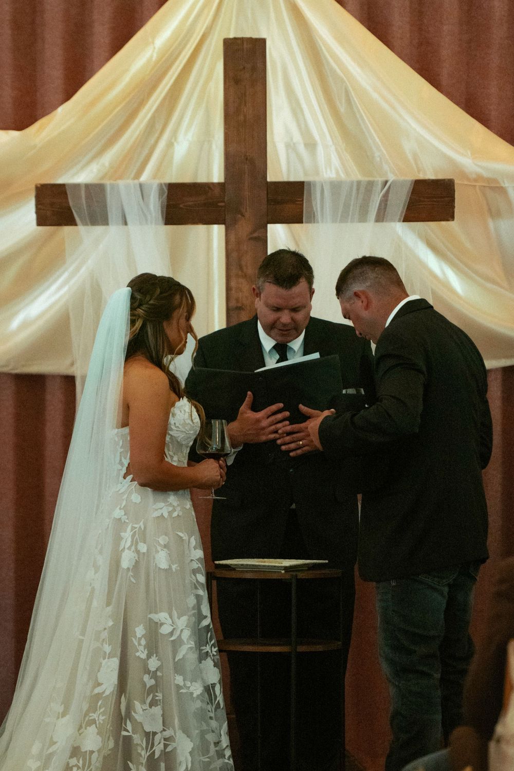 Bride and groom exchanging vows at altar with wooden cross and white draping during church wedding ceremony.