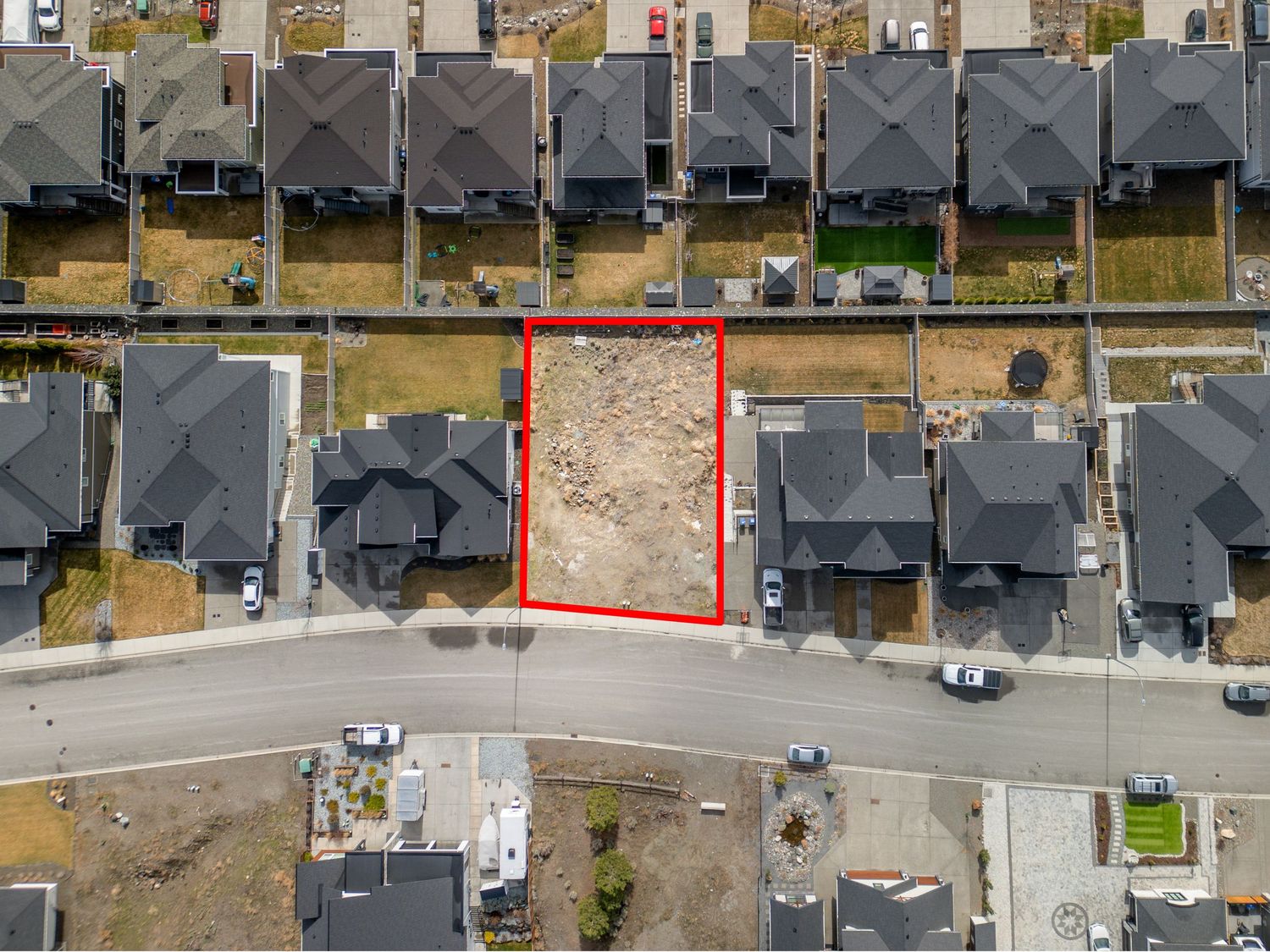 Aerial drone view of a vacant residential lot outlined in red, surrounded by modern homes in a suburban neighborhood.