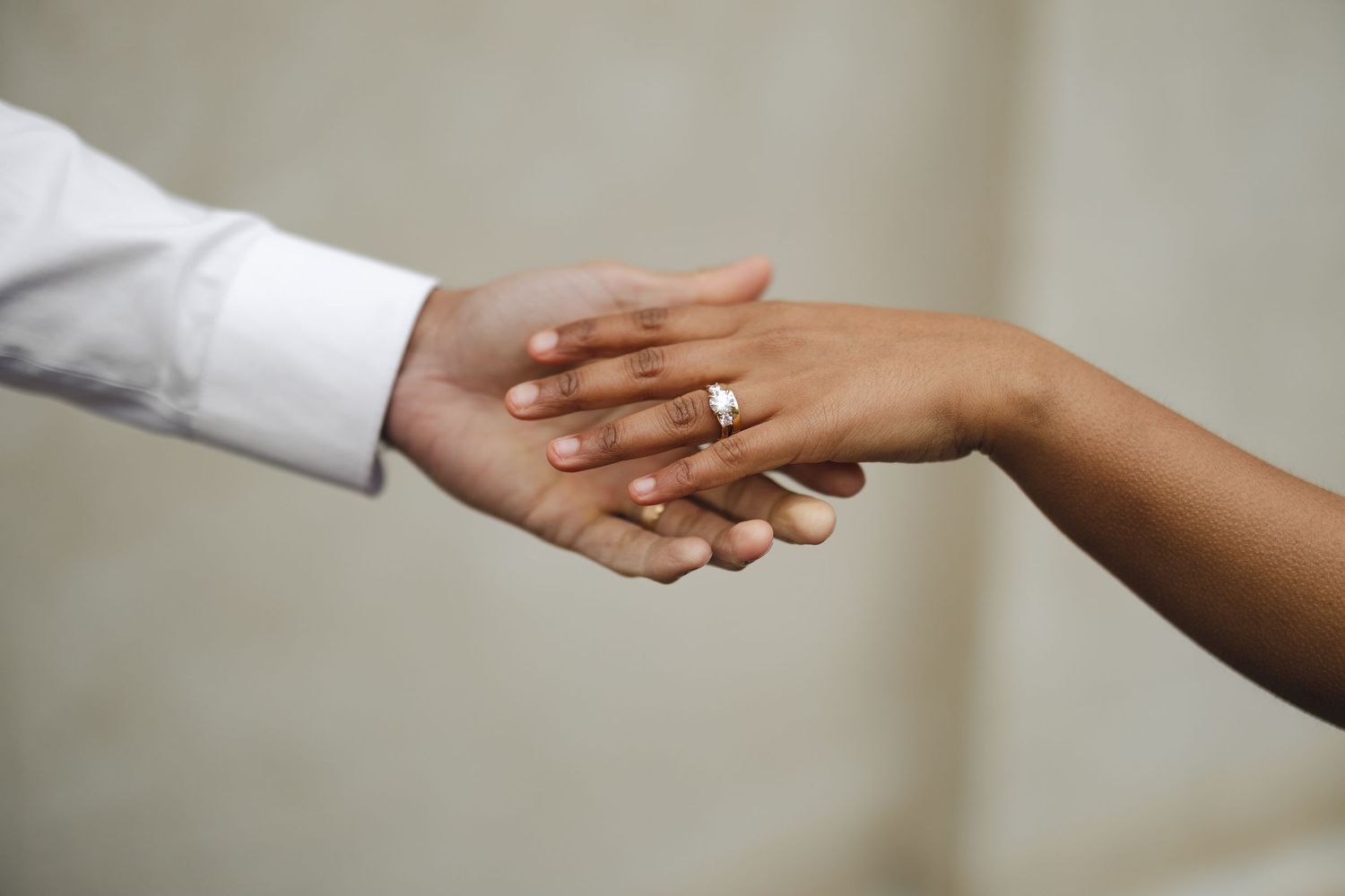 Close-up of an interracial couple holding hands, woman wearing a diamond engagement ring, symbolizing love and commitment.