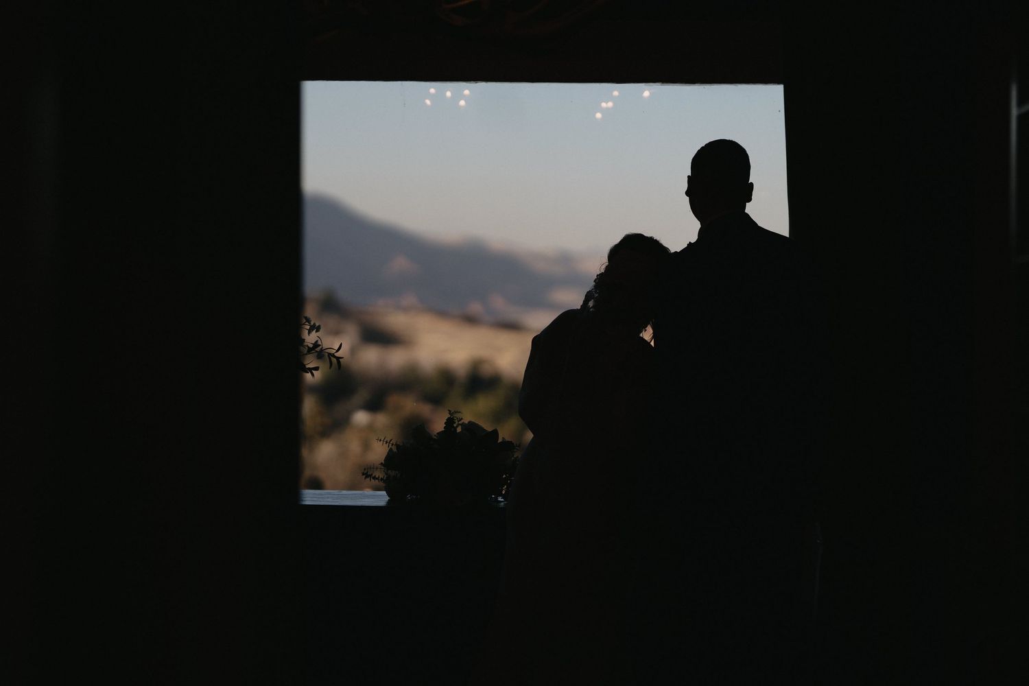 Silhouette of a couple embracing in a doorway with scenic mountain landscape at golden hour.