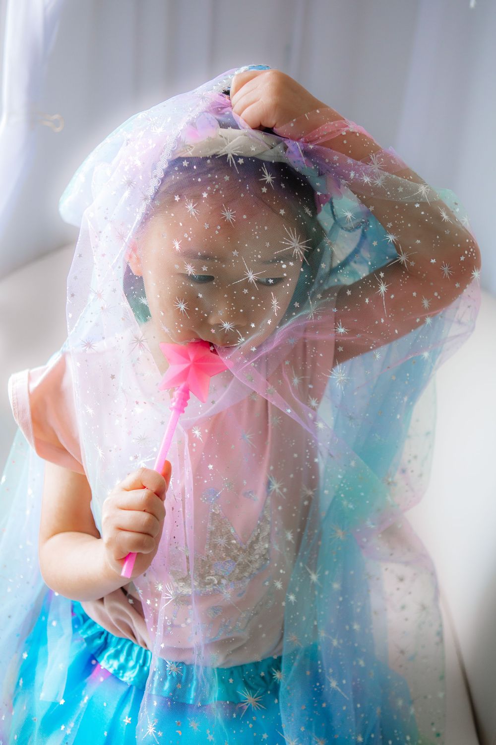 A figure in a sparkly pink and blue tulle dress twirls in front of a white backdrop, creating a dreamy ethereal effect.