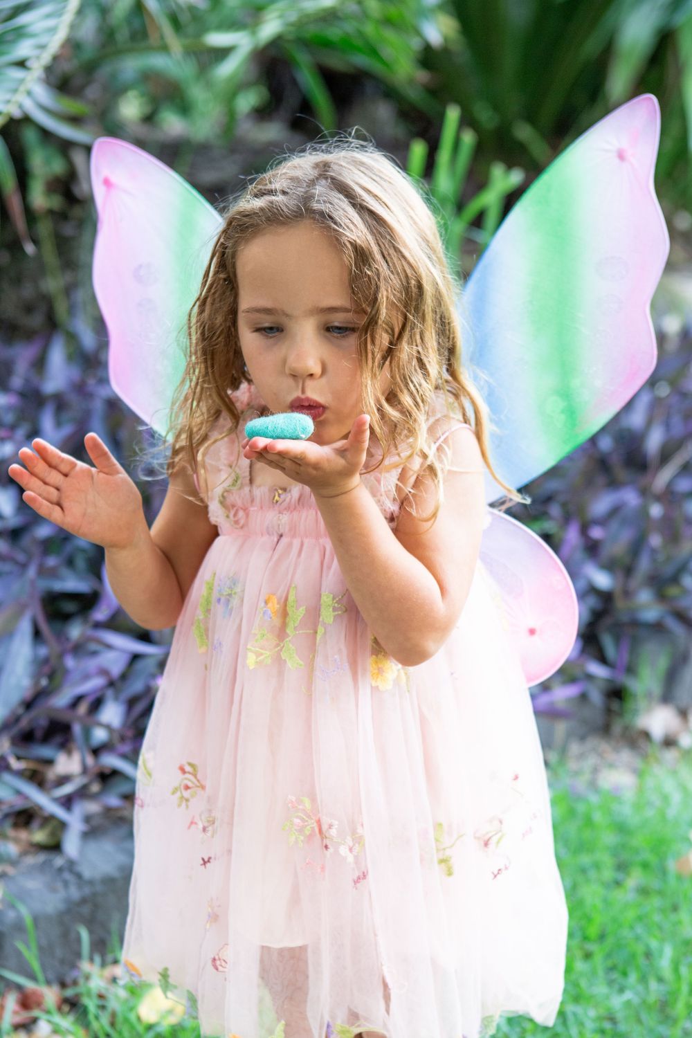 A young fairy in a delicate pink dress and wings dances joyfully in a lush garden.