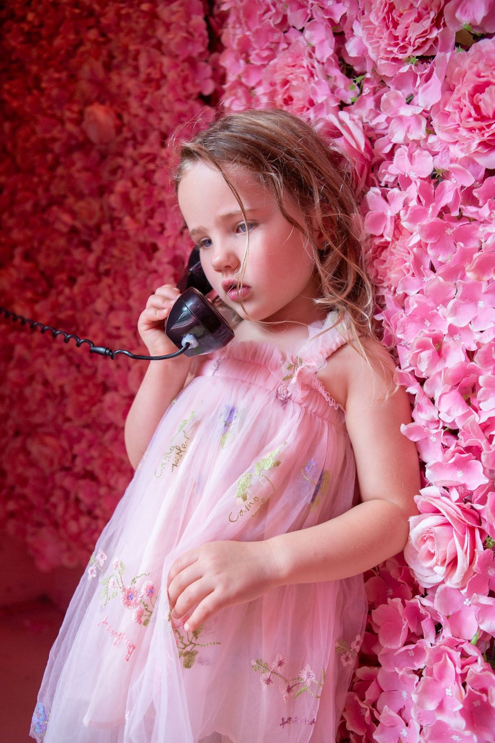 A child in a pink tulle dress poses against a backdrop of vibrant pink floral decorations.