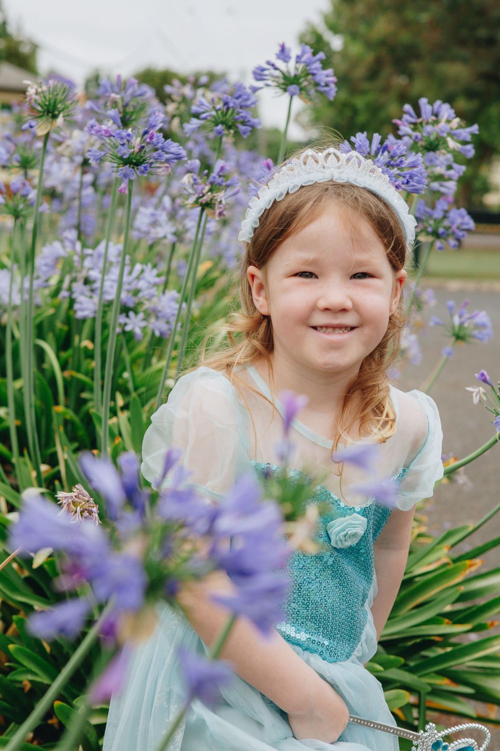 A magical fairy-themed photo series with purple agapanthus flowers and a turquoise dress in a garden setting.