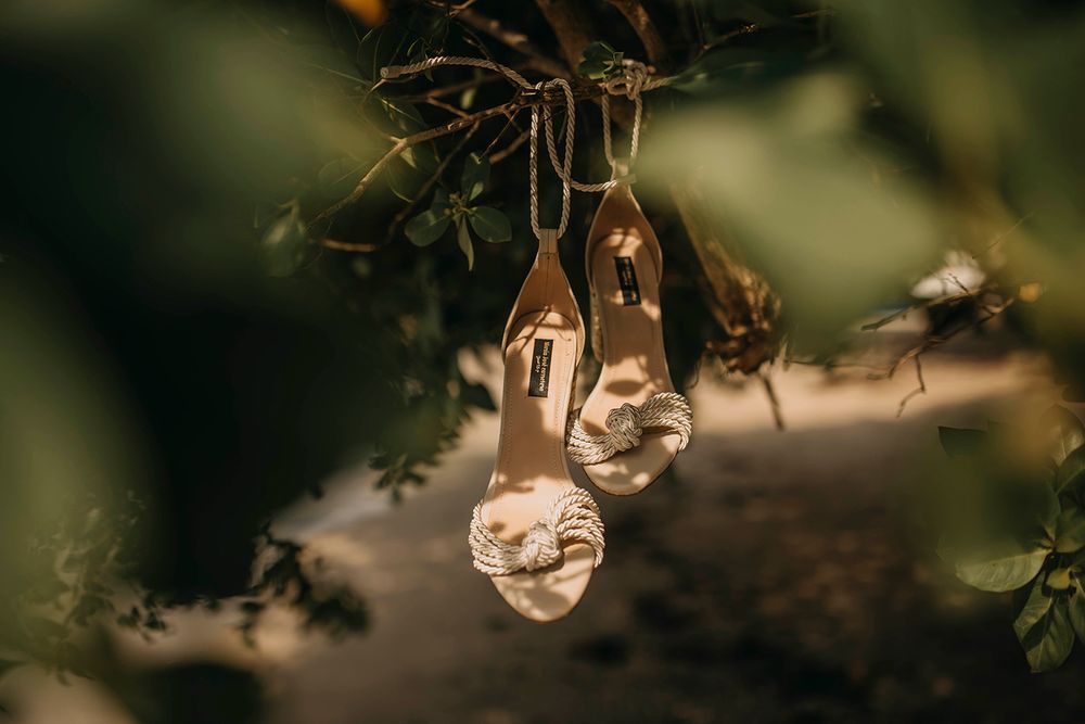Elegant white bridal heels hanging from tree branches in a dreamy outdoor wedding setting.