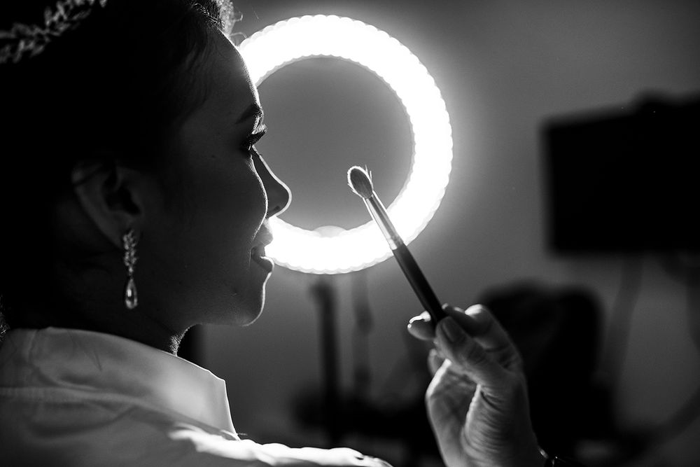 Bride applying makeup using a ring light in elegant black and white wedding preparation photo.