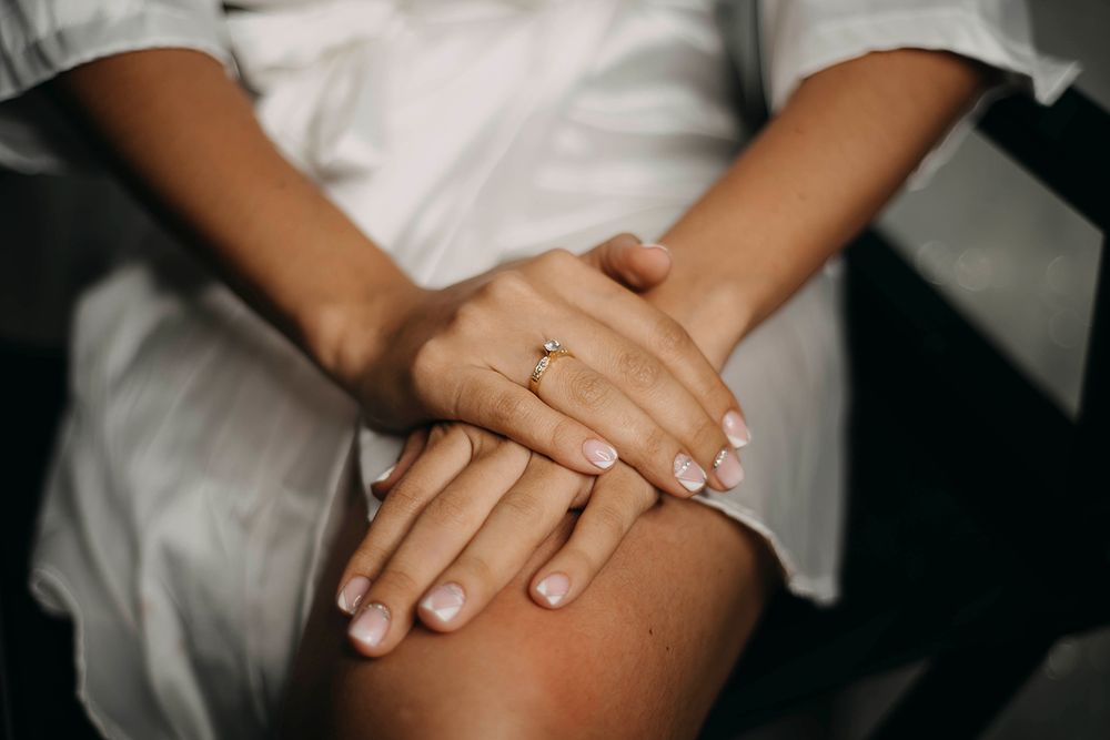 Close-up of bride's hands wearing a gold solitaire engagement ring with neutral manicured nails.