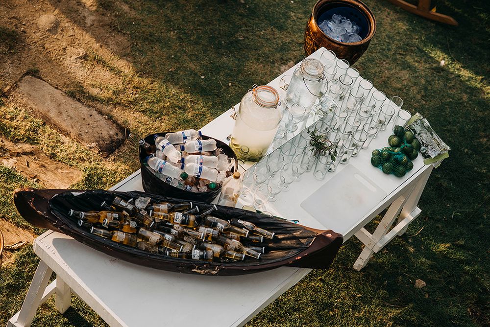 Outdoor bar setup with wine bottles in a wooden boat, charcuterie board, and glassware on a white table.