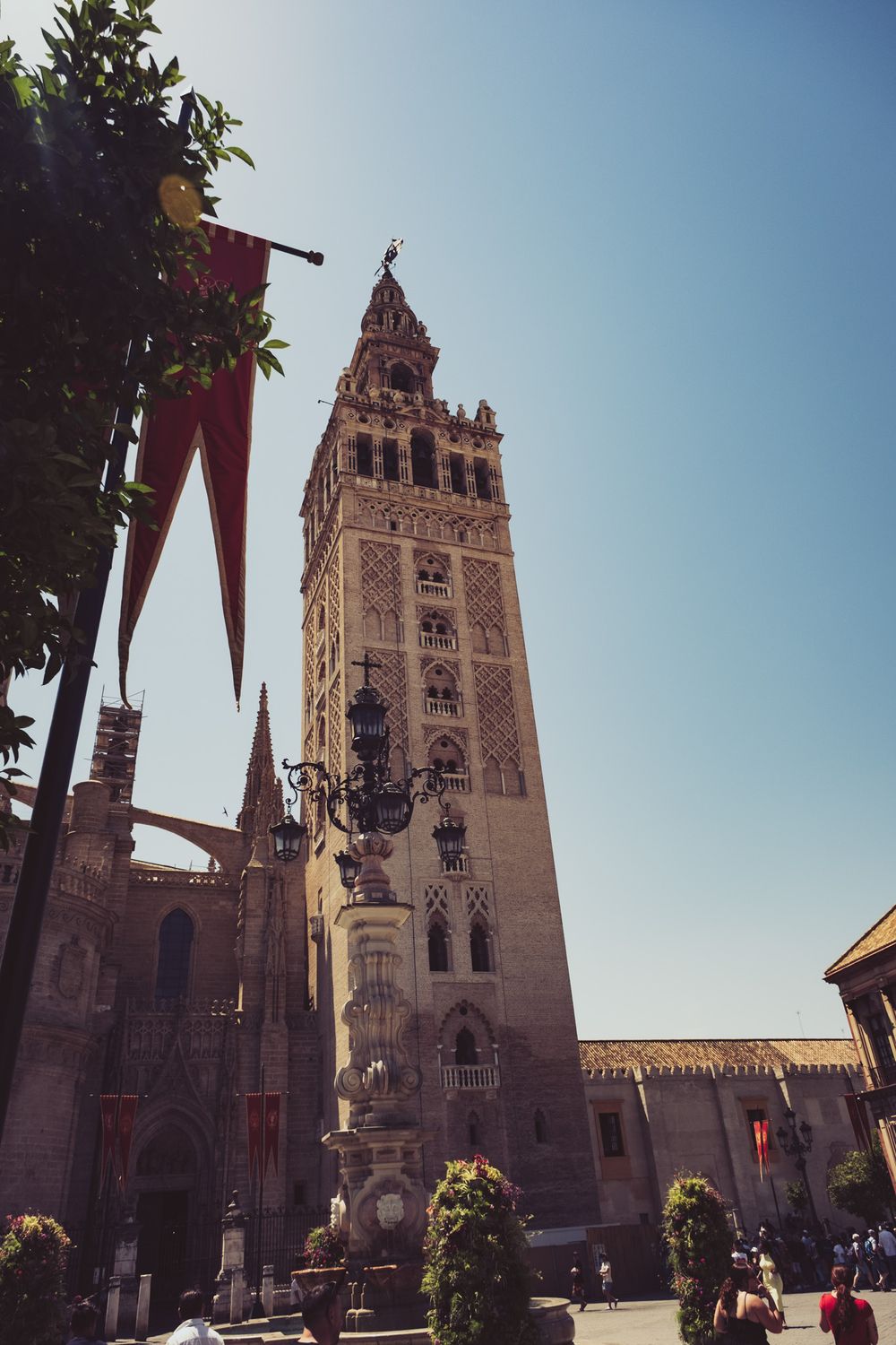 La Giralda bell tower of Seville Cathedral with red banners and ornate street lamp, Spain.
